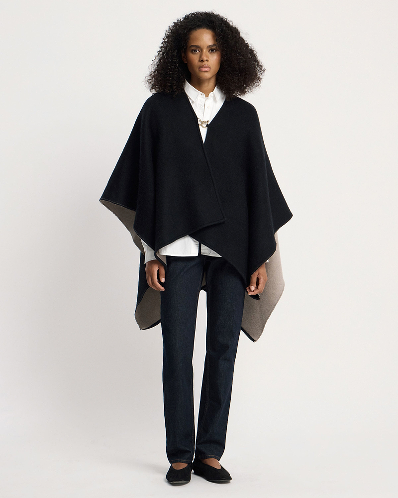 Woman wearing otter and black woven kite cape over white shirt and jeans.