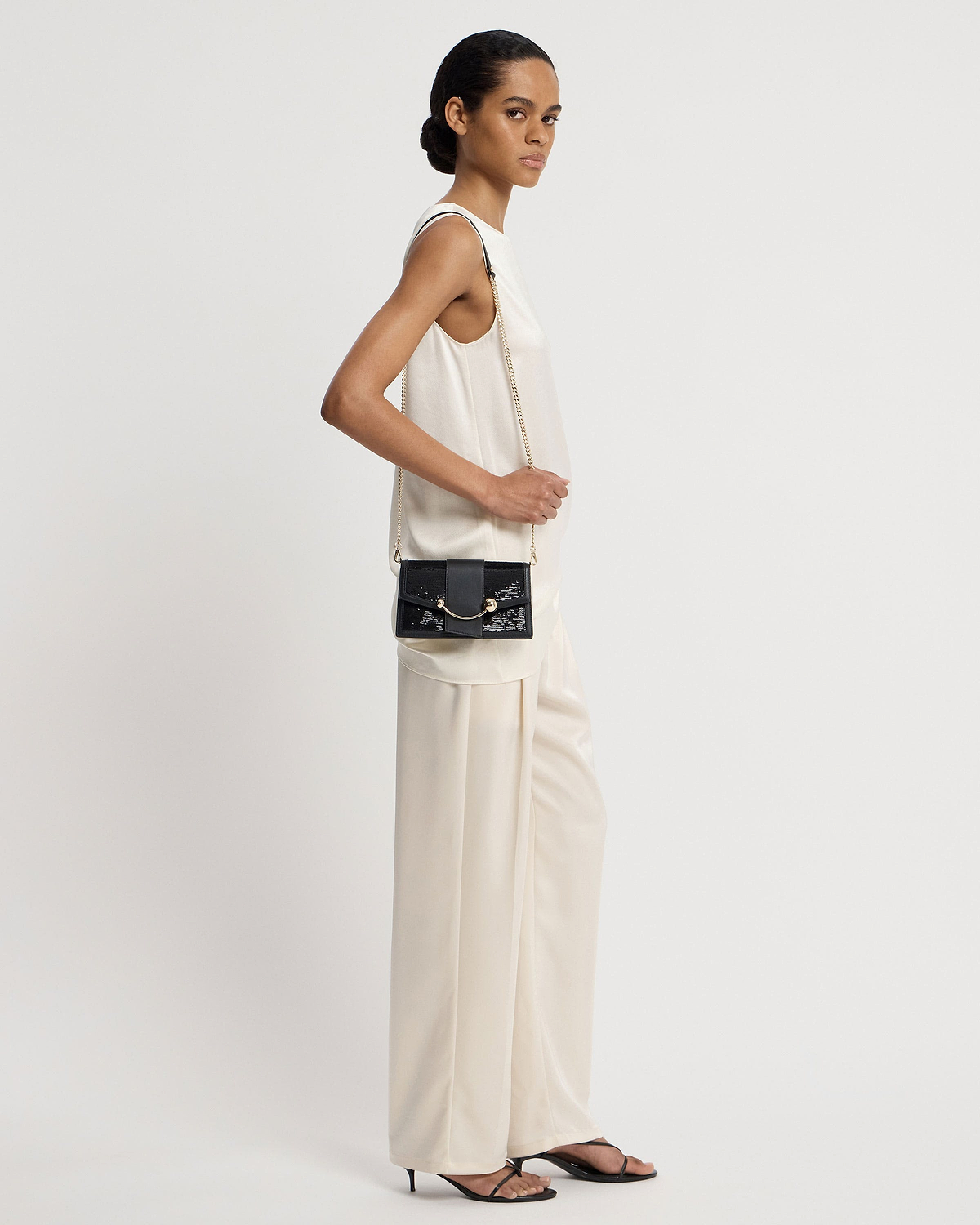 Model wearing a black sequin crescent-on-a-chain shoulder bag with gold chain.