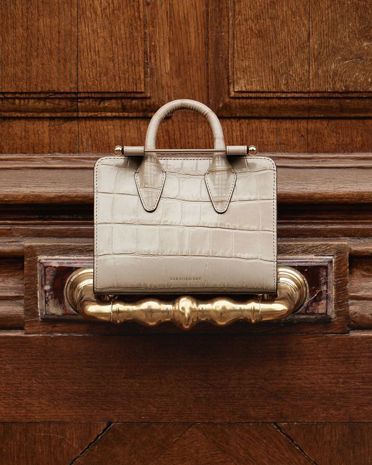 Strathberry nano tote in croc leather on a wooden door handle.