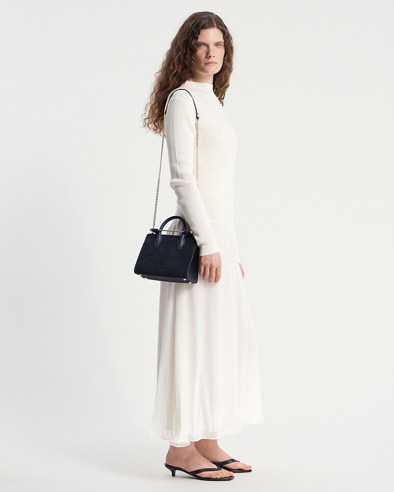 Woman in cream dress carrying navy suede mini tote with gold chain strap.