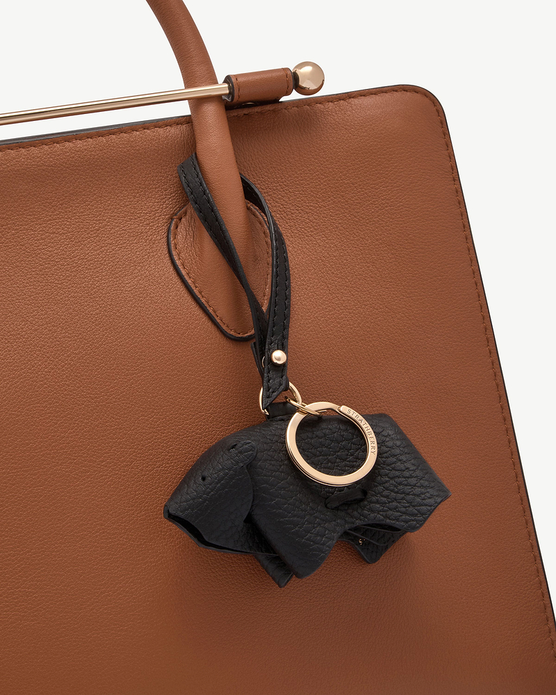 Black leather bear bag charm hanging from brown leather handbag handle with gold ring