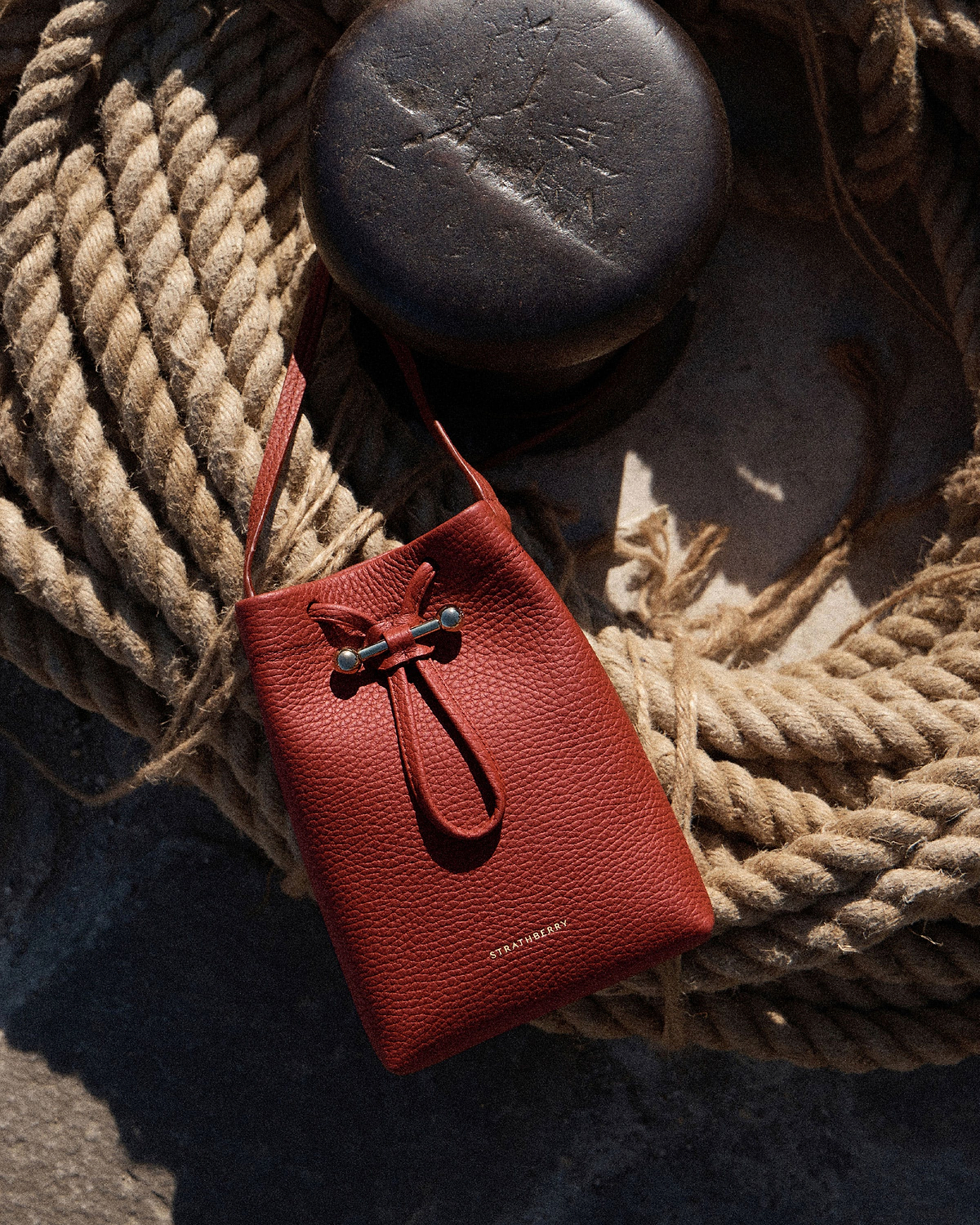 Strathberry Osette midi pouch in Levanto red resting on coiled rope.