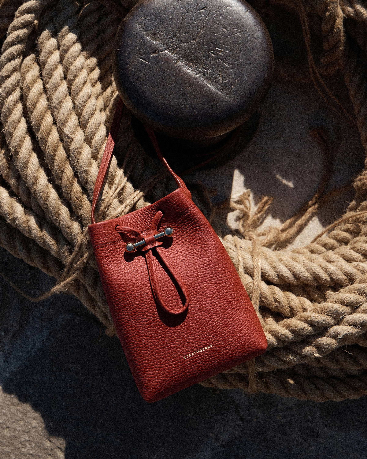 Strathberry Osette midi pouch in Levanto red resting on coiled rope.
