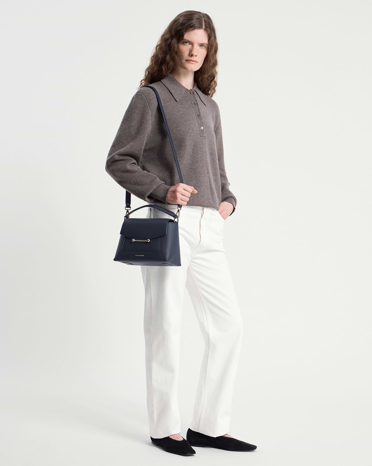 Model wearing grey sweater and white trousers holding navy Strathberry mosaic bag