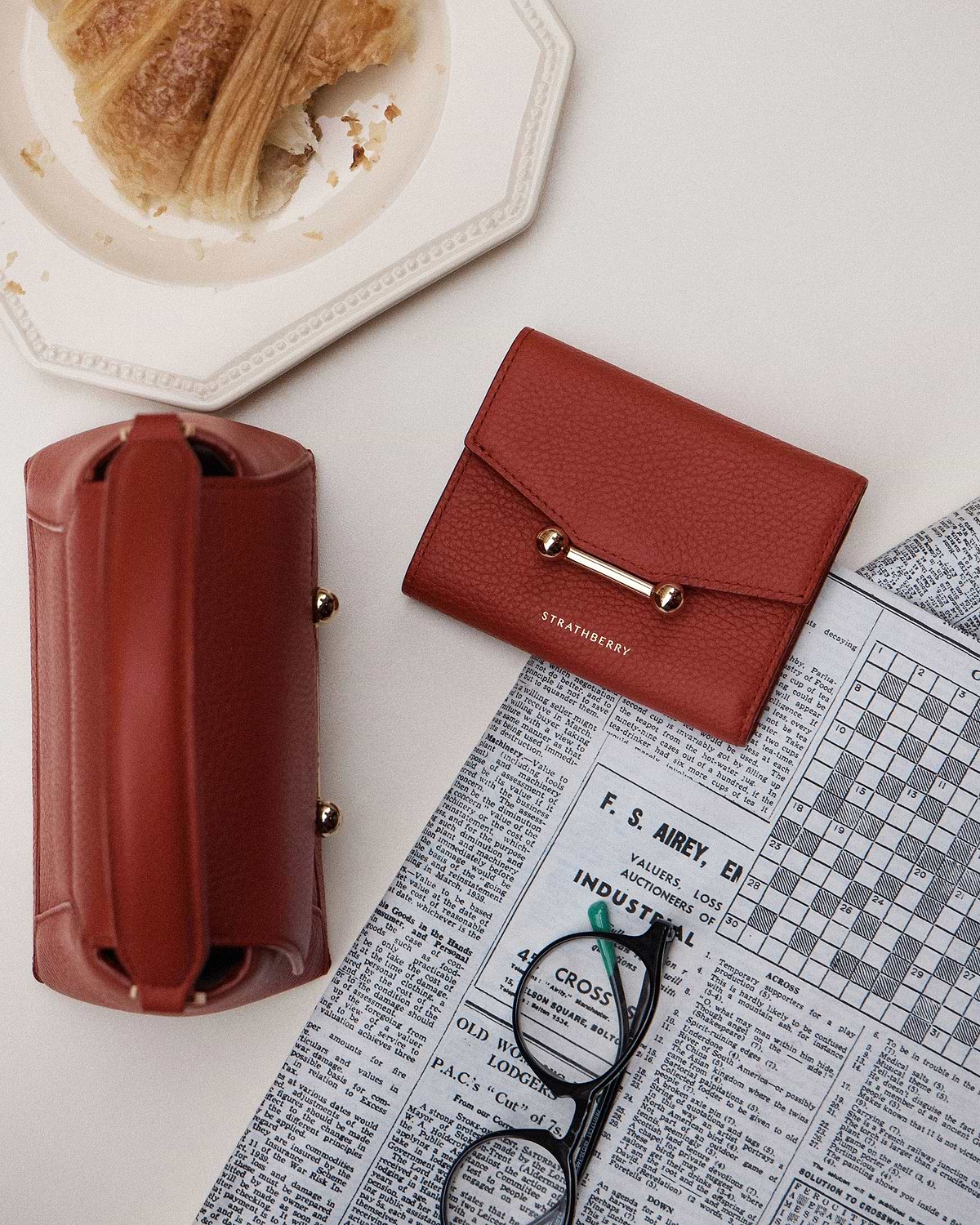 Levanto red mosaic trifold wallet by Strathberry with leather pouch, glasses and croissant.