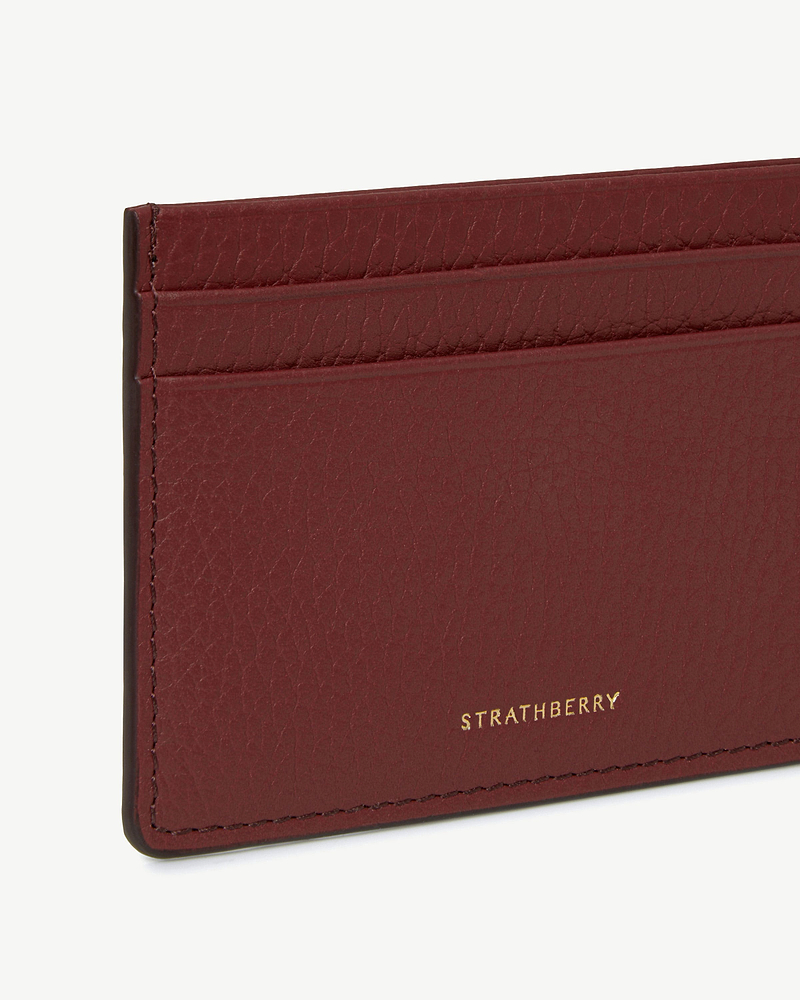 Oxblood leather three-slot cardholder with gold Strathberry logo and textured finish.