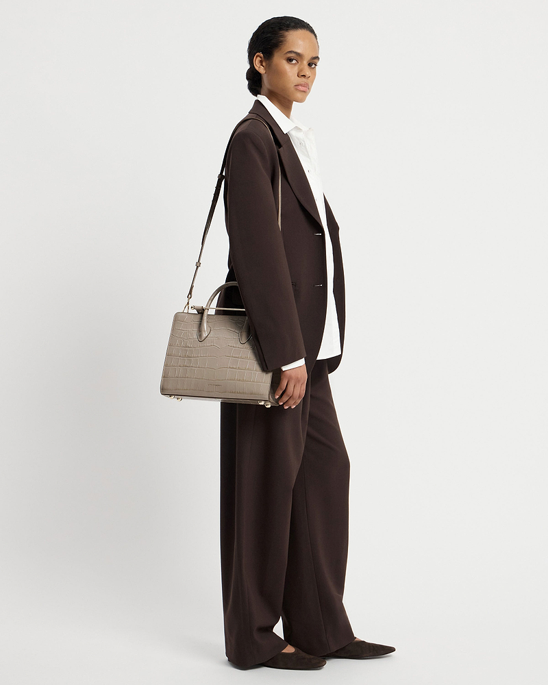 Woman in brown suit carrying a croc-effect midi tote bag at her side.