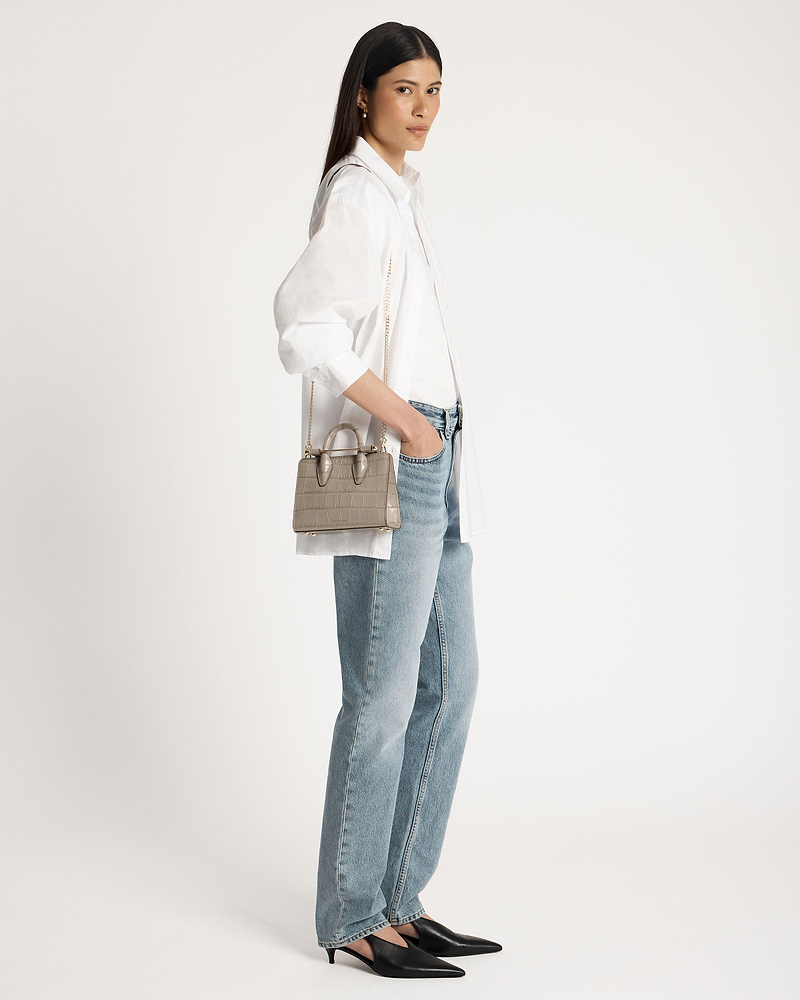 Woman wearing white shirt and jeans carrying a croc nano tote bag.