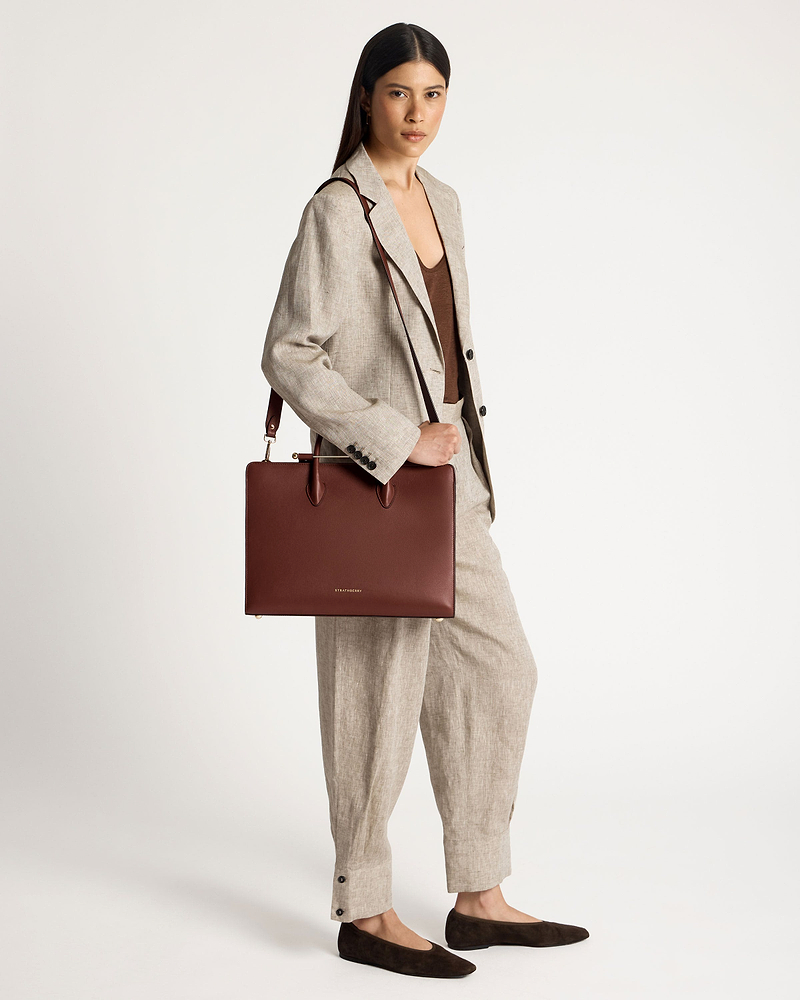 Woman in beige suit holding a walnut Strathberry tote bag by her shoulder.