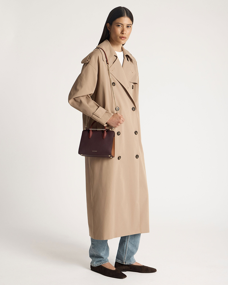 Model in beige trench coat holding burgundy, chestnut and walnut mini tote bag.
