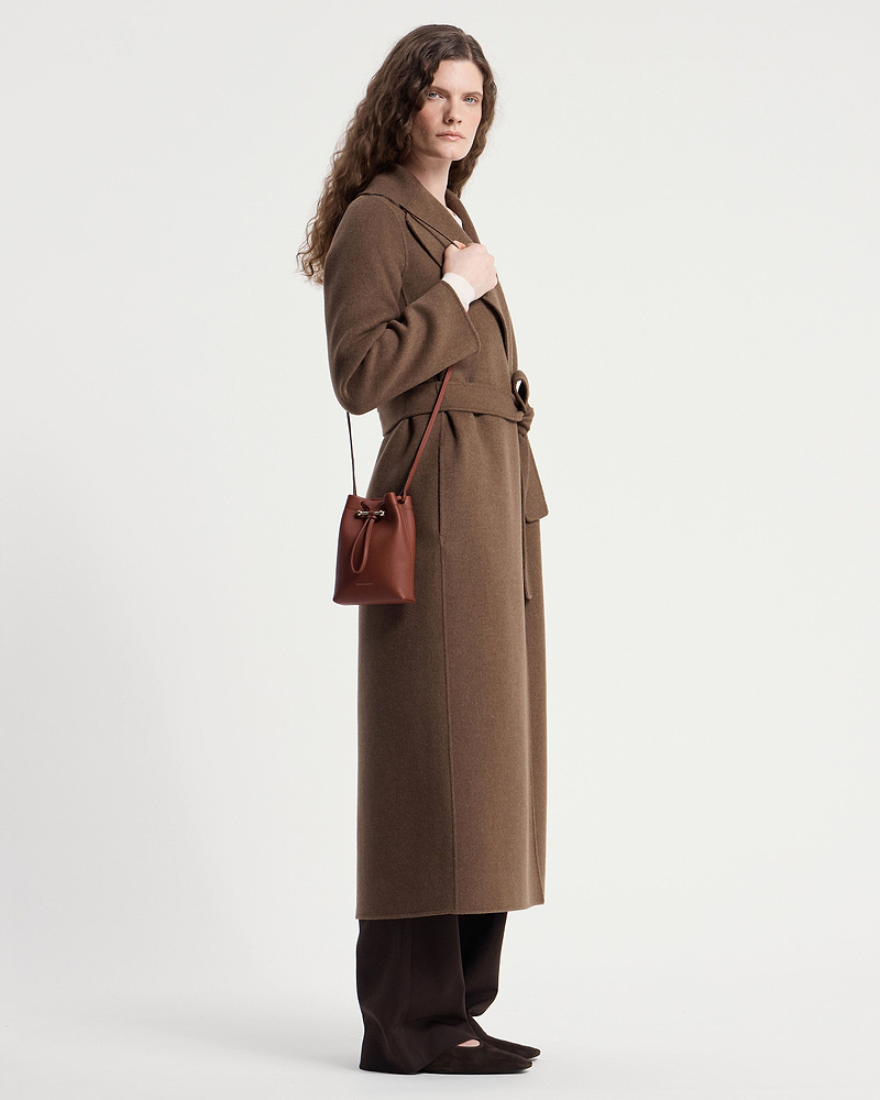 Model wearing a brown coat carrying a walnut leather midi pouch crossbody.