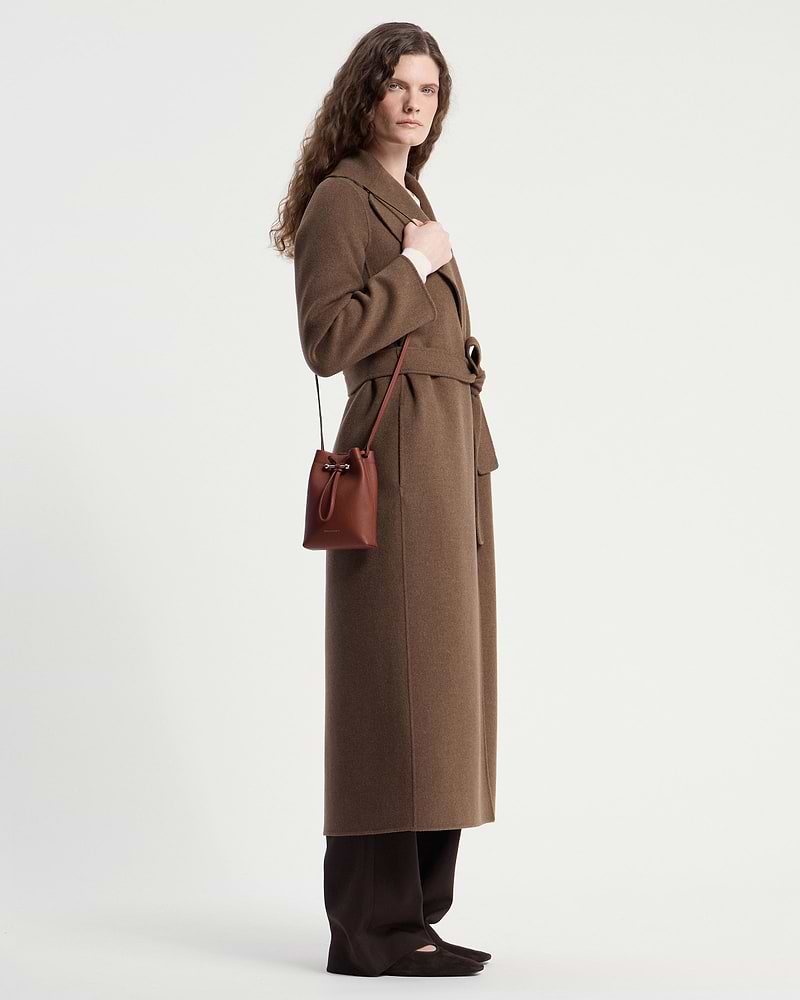 Model wearing a brown coat carrying a walnut leather midi pouch crossbody.