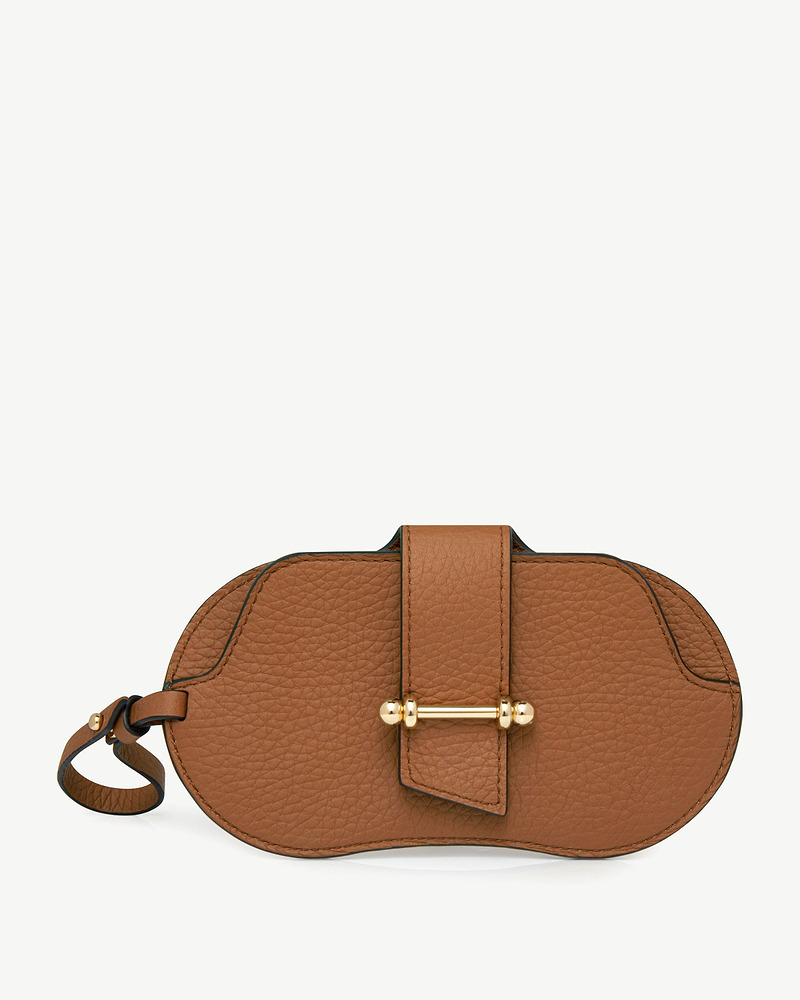 Tan pebbled leather sunglasses case with central strap, gold-bar closure and wrist loop.