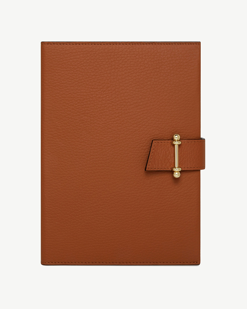 Tan leather notebook with gold bar clasp and pebble-grain texture.