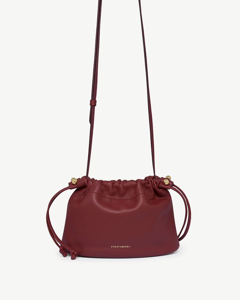 Strathberry Charlotte drawstring bag in oxblood leather with long shoulder strap.