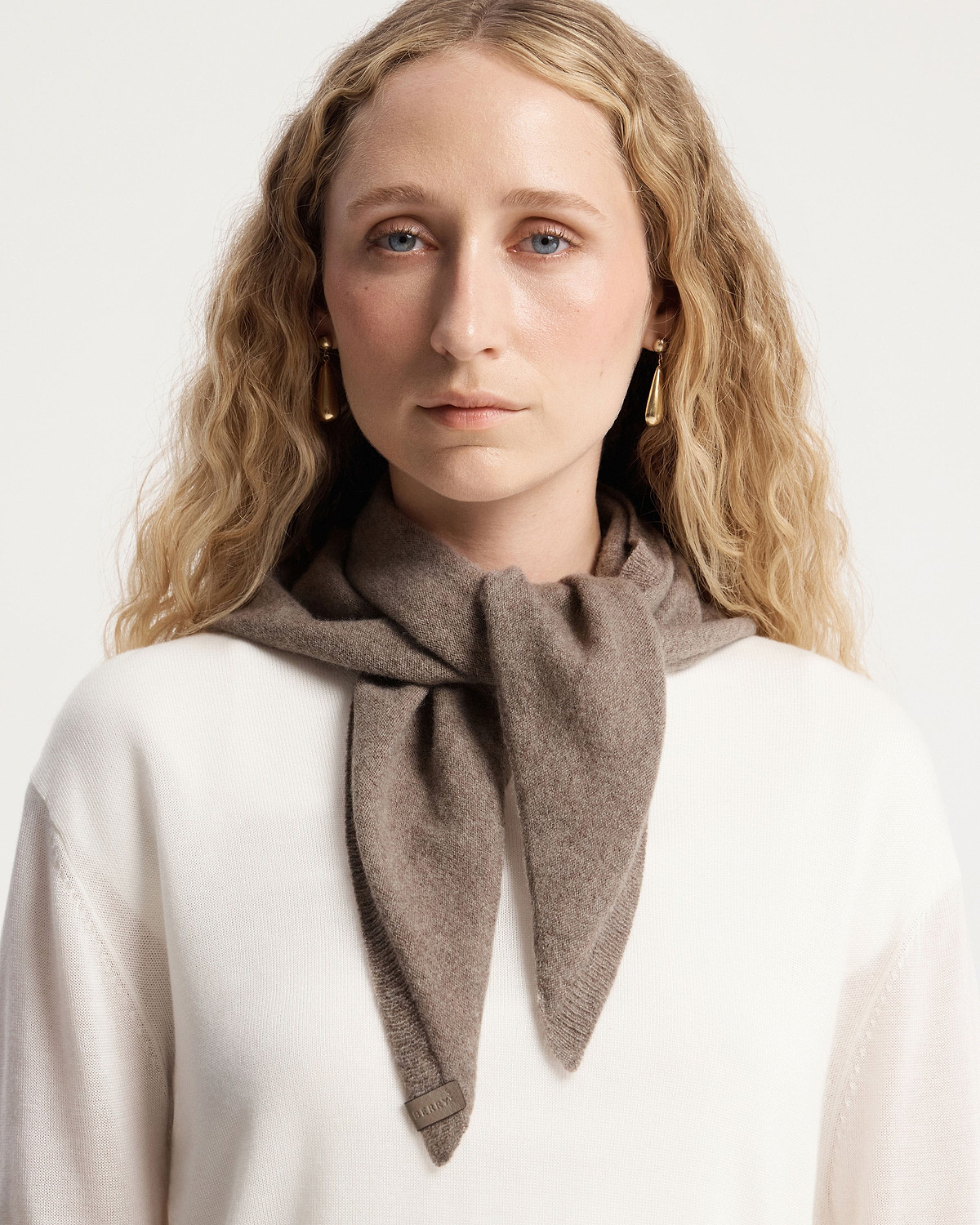 Model wearing pebble cashmere bandana tied at front over white jumper.