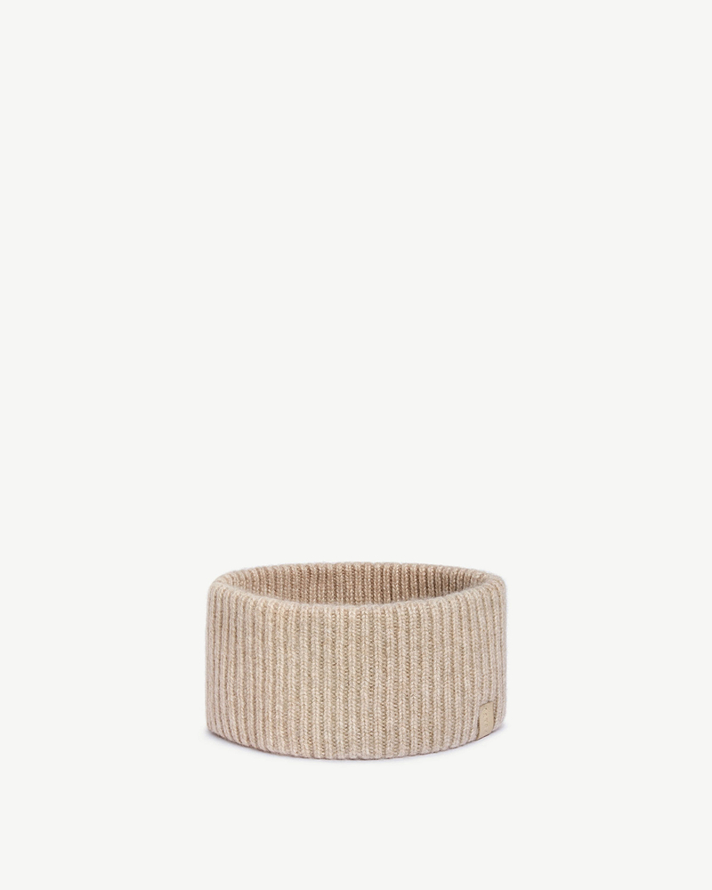 Oat ribbed cashmere headband folded upright with small leather tag on white background.