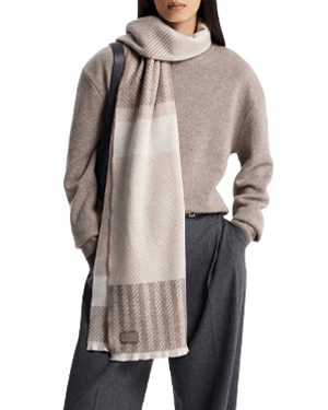 Model wearing taupe tartan cashmere scarf over beige jumper and grey trousers.