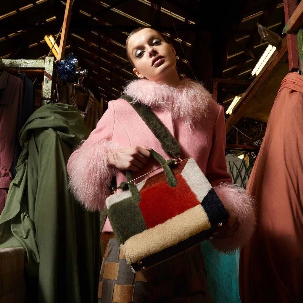 A woman in a pink coat holding a multicolored purse