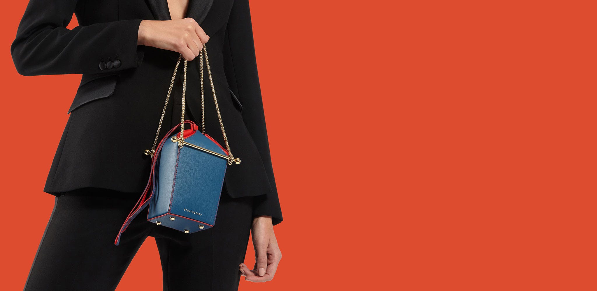 A woman in a black suit holding a blue and red purse