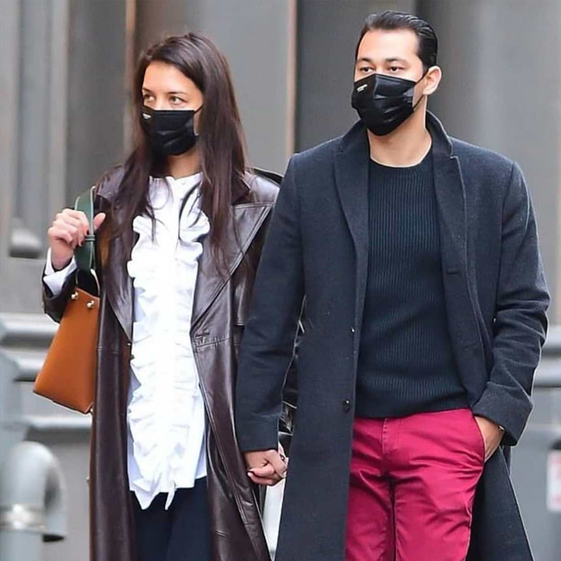 A man and a woman walking down a street wearing face masks