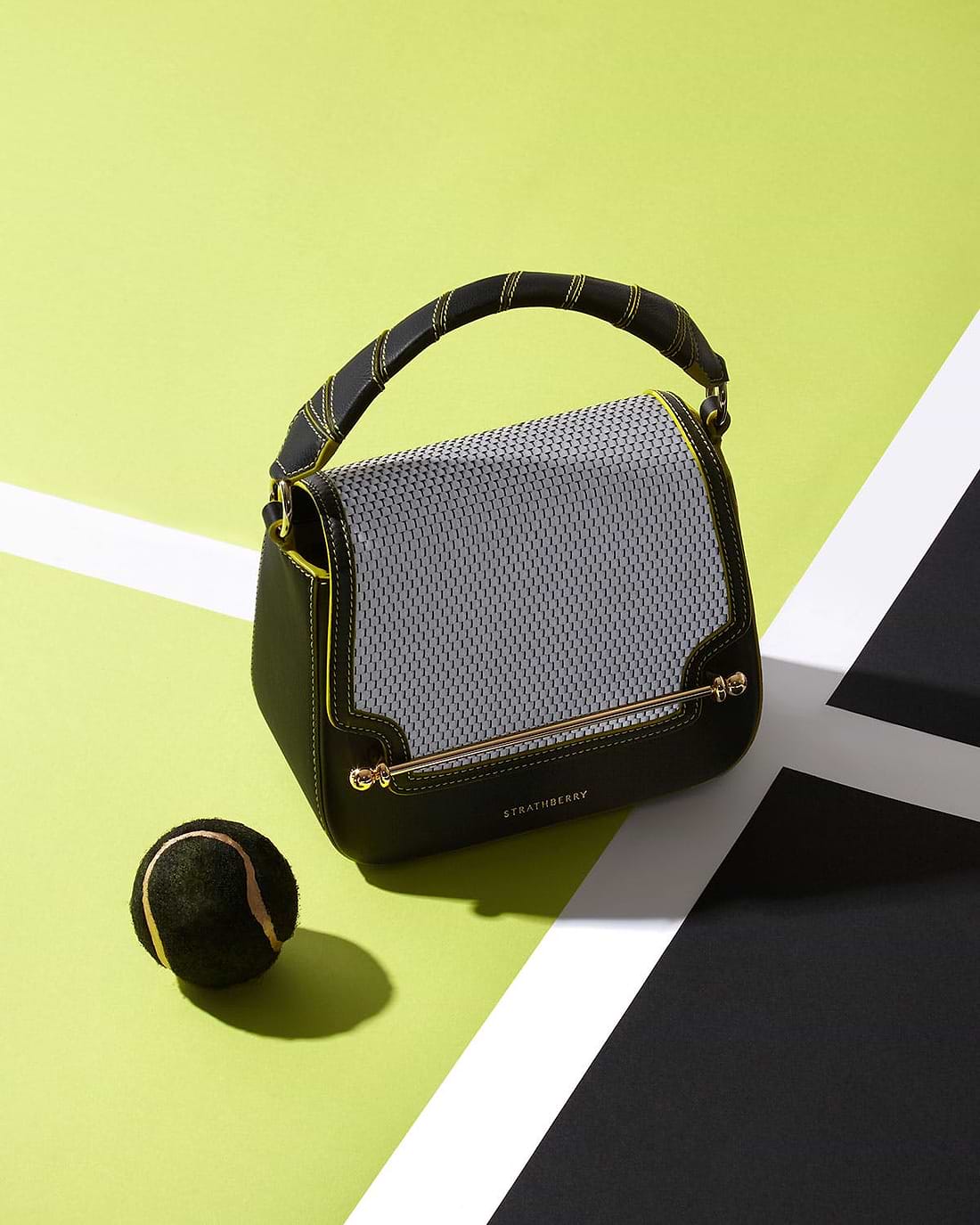 A tennis ball sitting next to a black and white purse