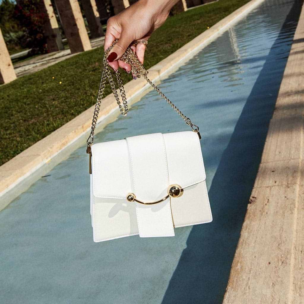 A person holding a white purse over a body of water