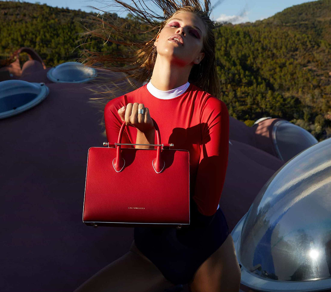 A woman holding a red purse in front of her face