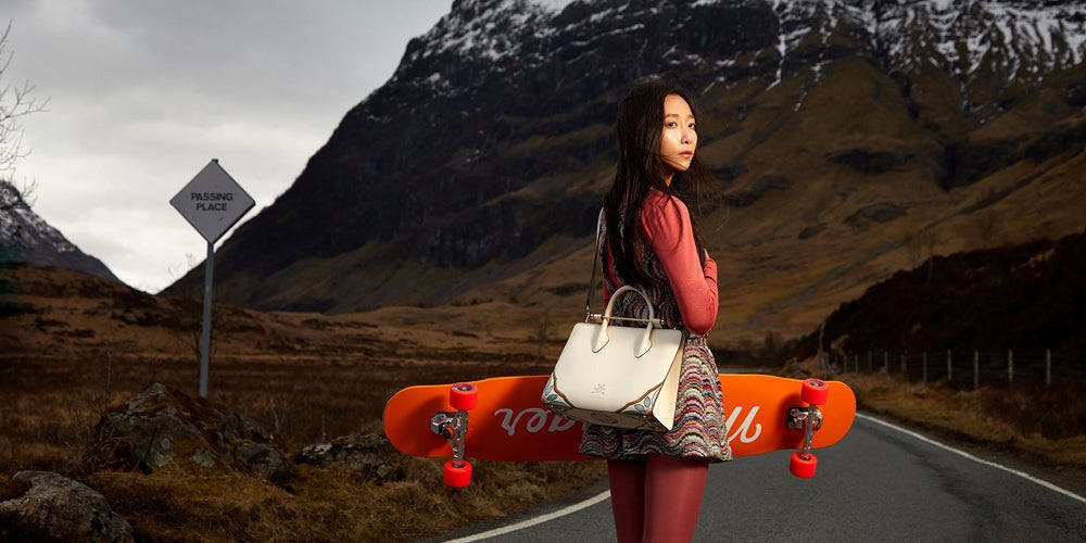 A woman holding a skateboard on the side of a road
