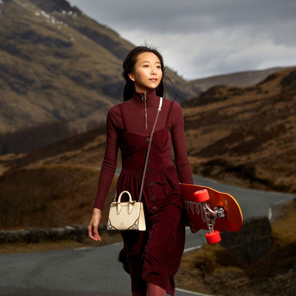 A woman walking down a road holding a skateboard