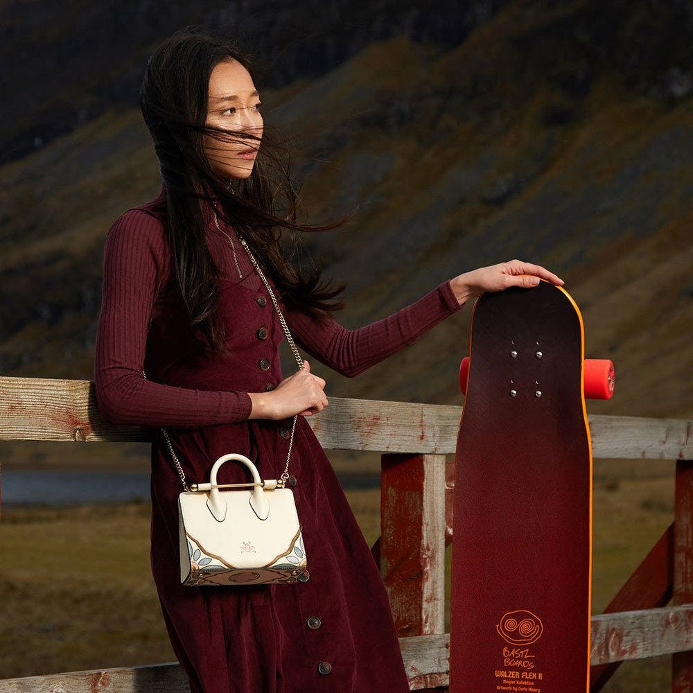 A woman holding a skateboard next to a wooden fence