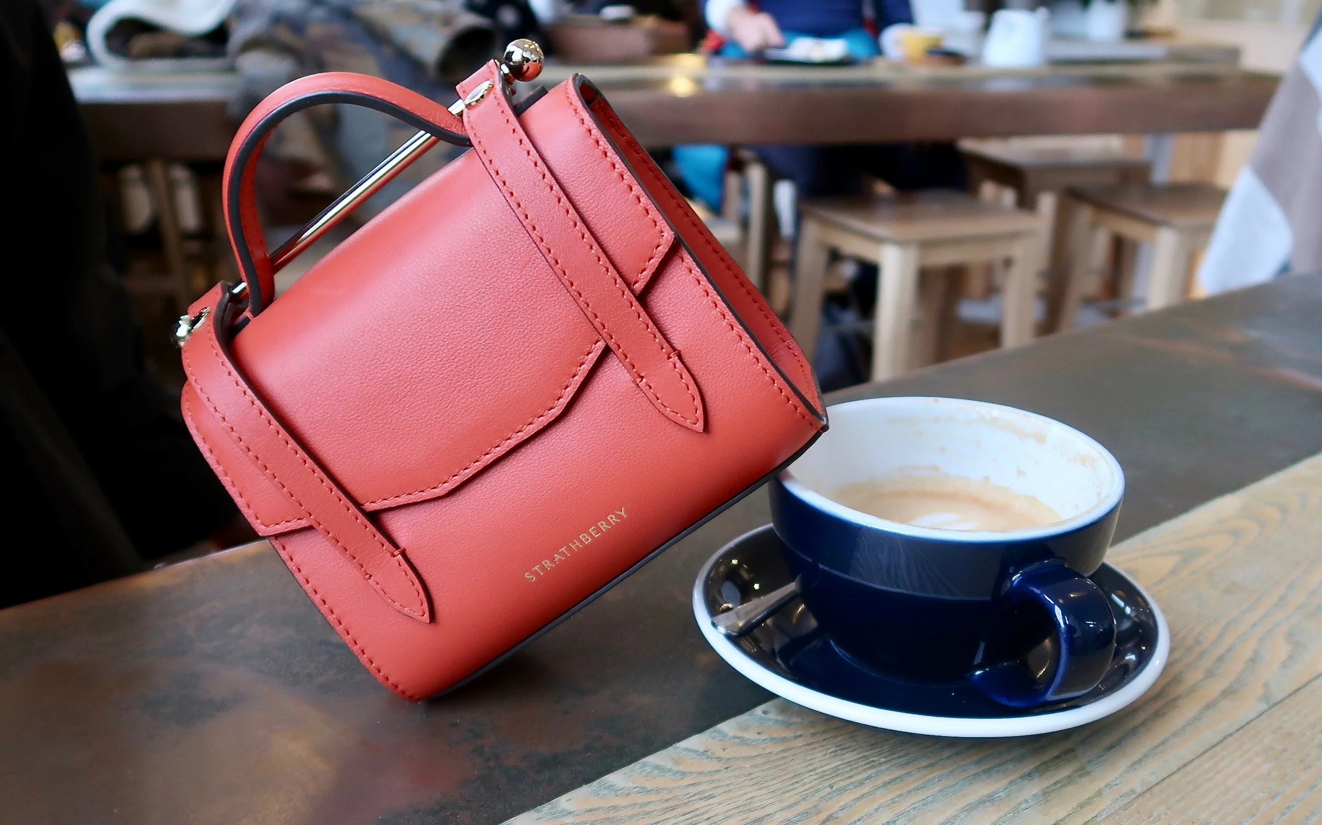 A red purse sitting on top of a table next to a cup of coffee
