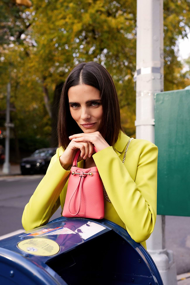 A woman leaning on a trash can holding a pink purse
