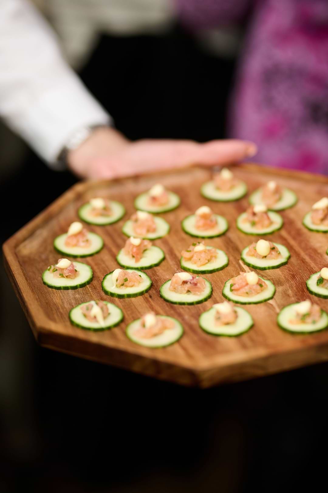 A person holding a wooden tray with cucumbers on it