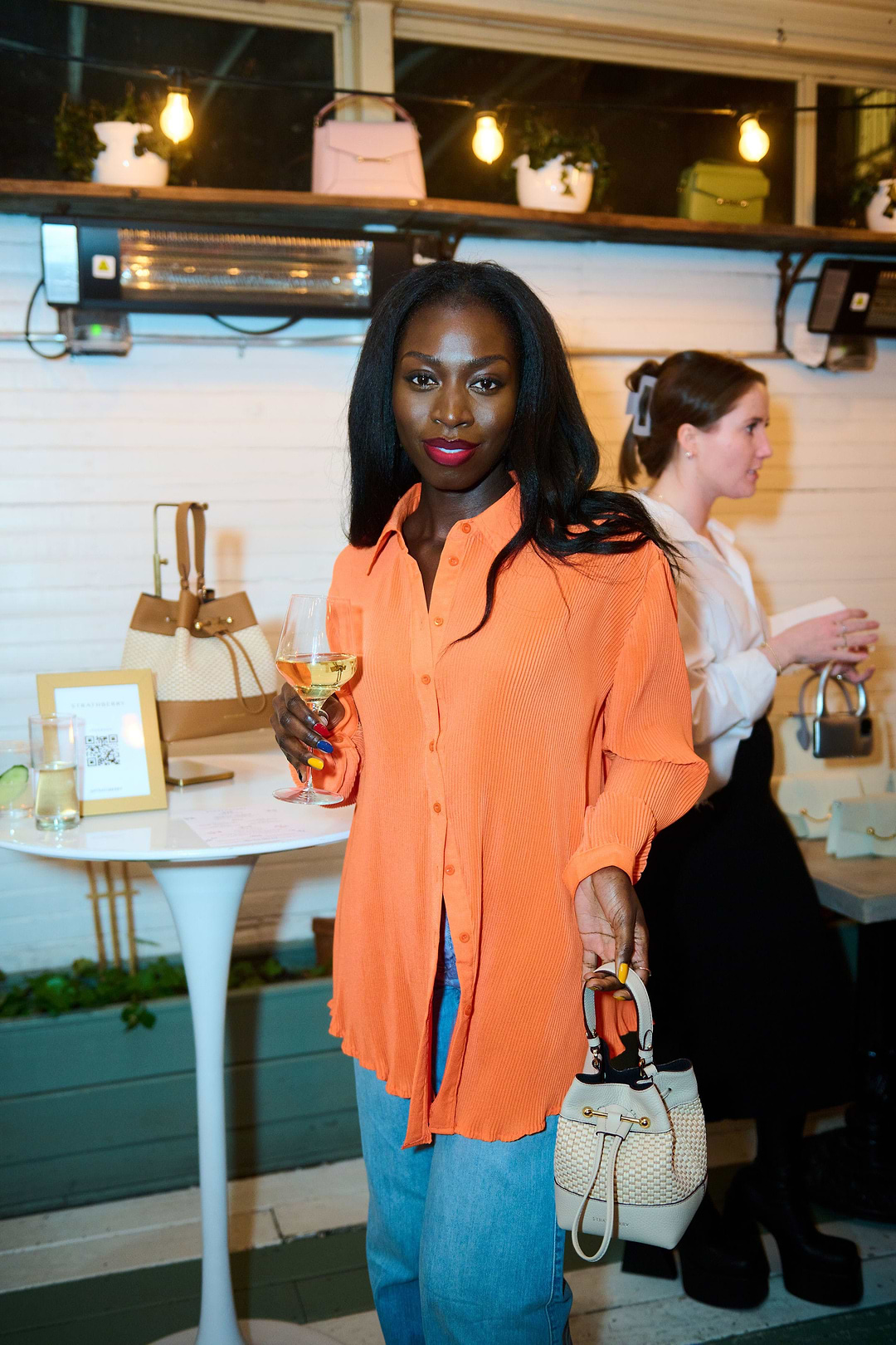 A woman in an orange shirt holding a white purse