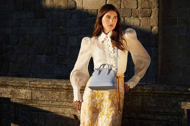 A woman standing next to a stone wall holding a purse
