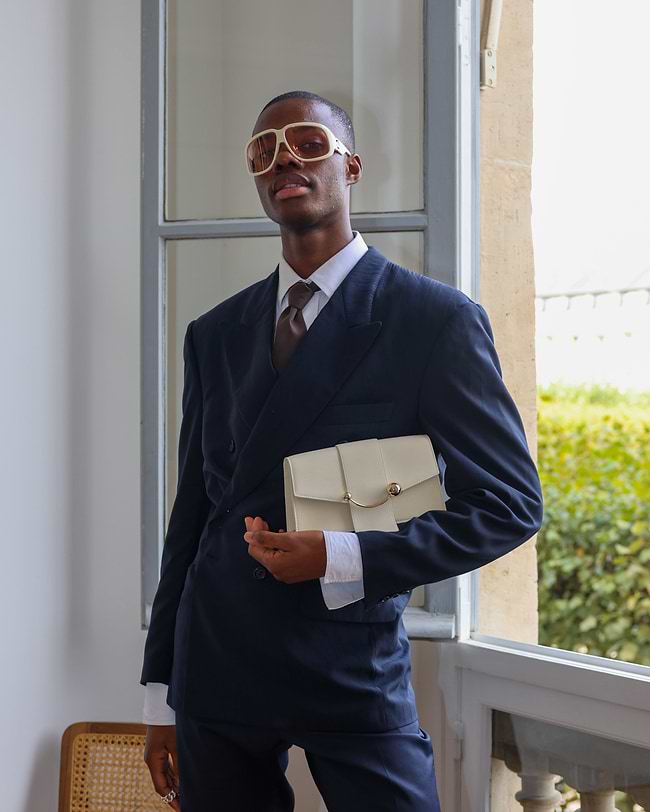 A man in a suit and sunglasses holding a purse