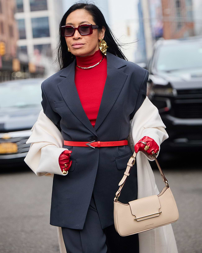 A woman in a red shirt and black suit carrying a beige purse