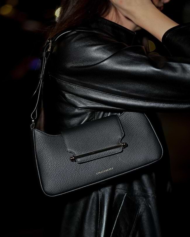 A woman in a black leather jacket holding a black purse