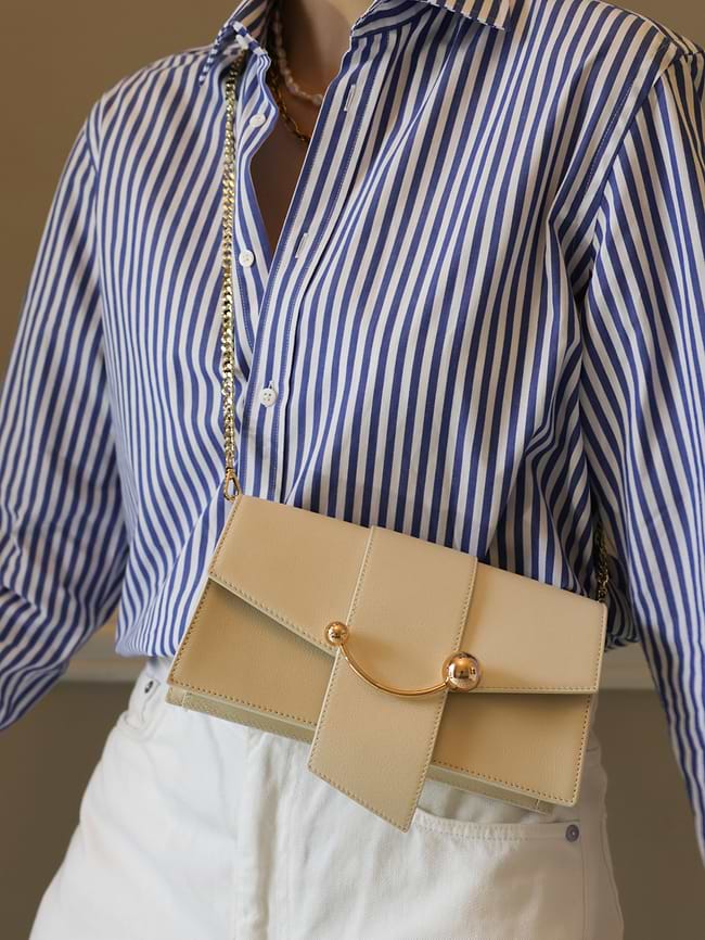 A woman wearing a blue and white striped shirt holding a tan purse