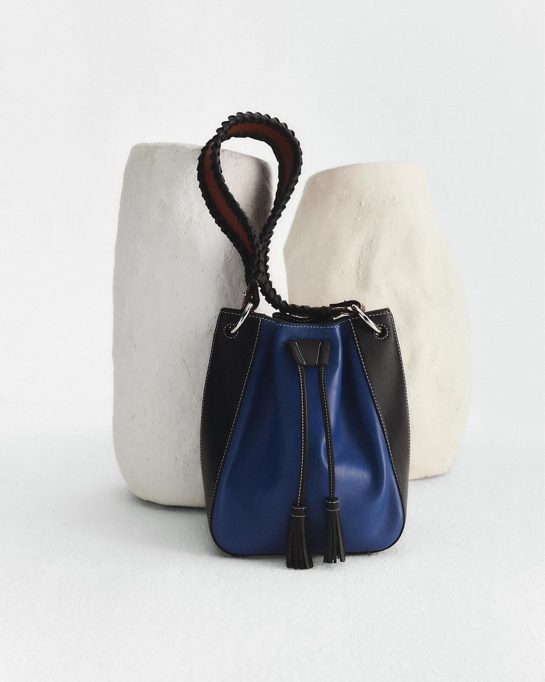 A black and blue purse sitting next to a white vase