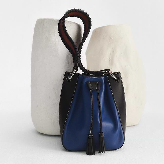 A black and blue purse sitting next to a white vase