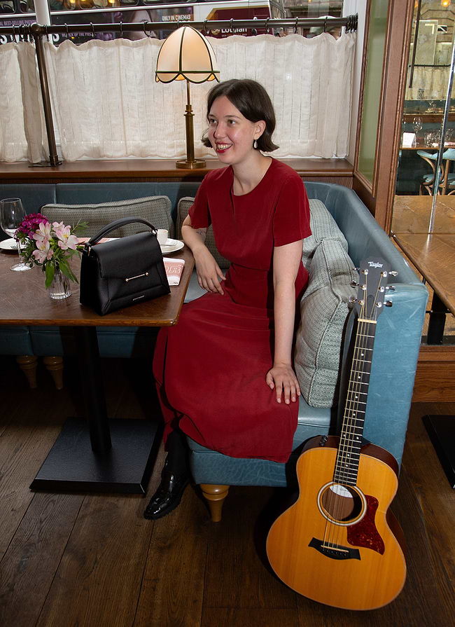 A woman in a red dress sitting at a table with a guitar