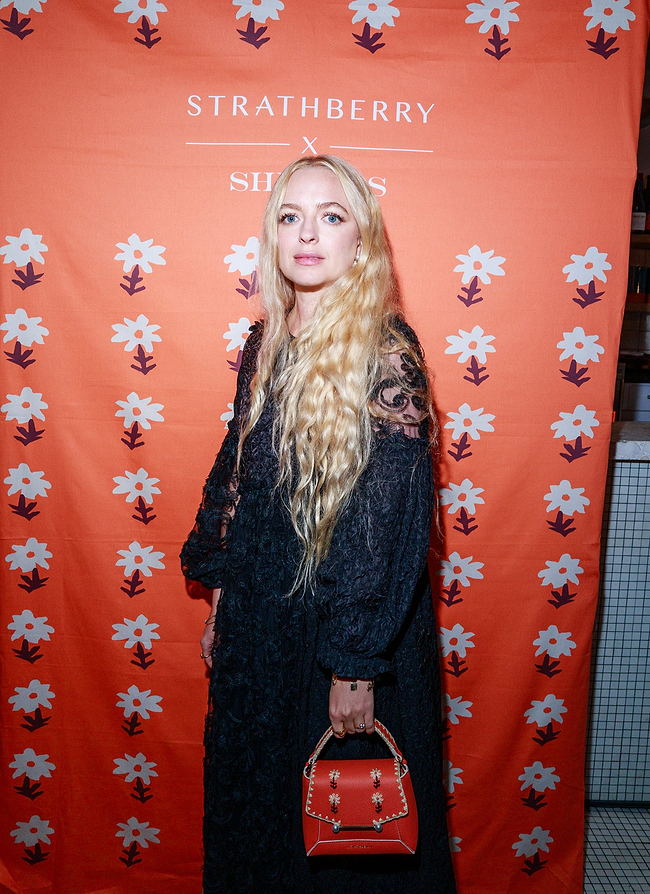 A woman with long blonde hair standing in front of a red backdrop