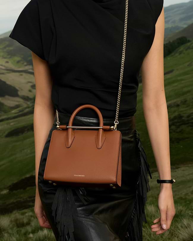 A woman in a black dress carrying a brown purse