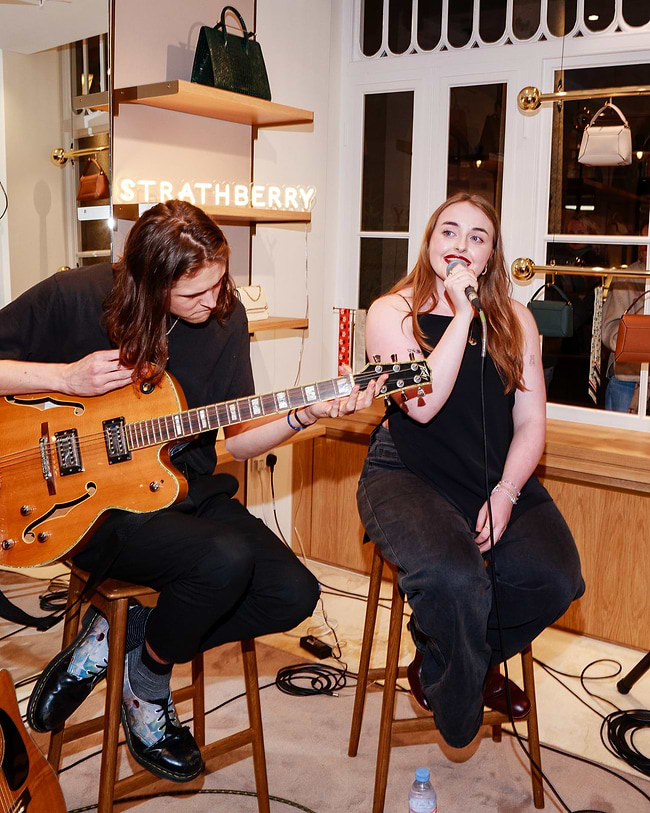 A woman sitting on a stool next to a man holding a guitar