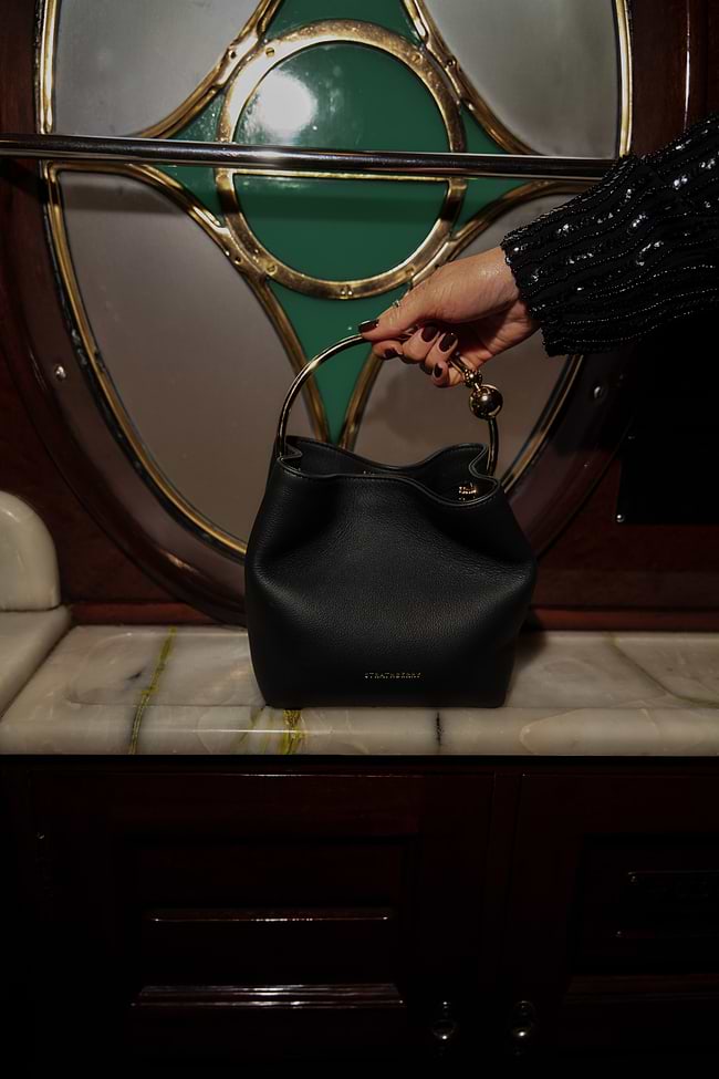 A person holding a black purse in front of a green door