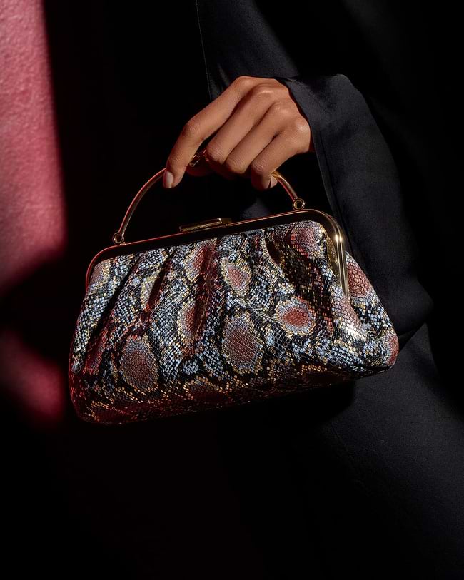 A woman's hand holding a snake skin purse