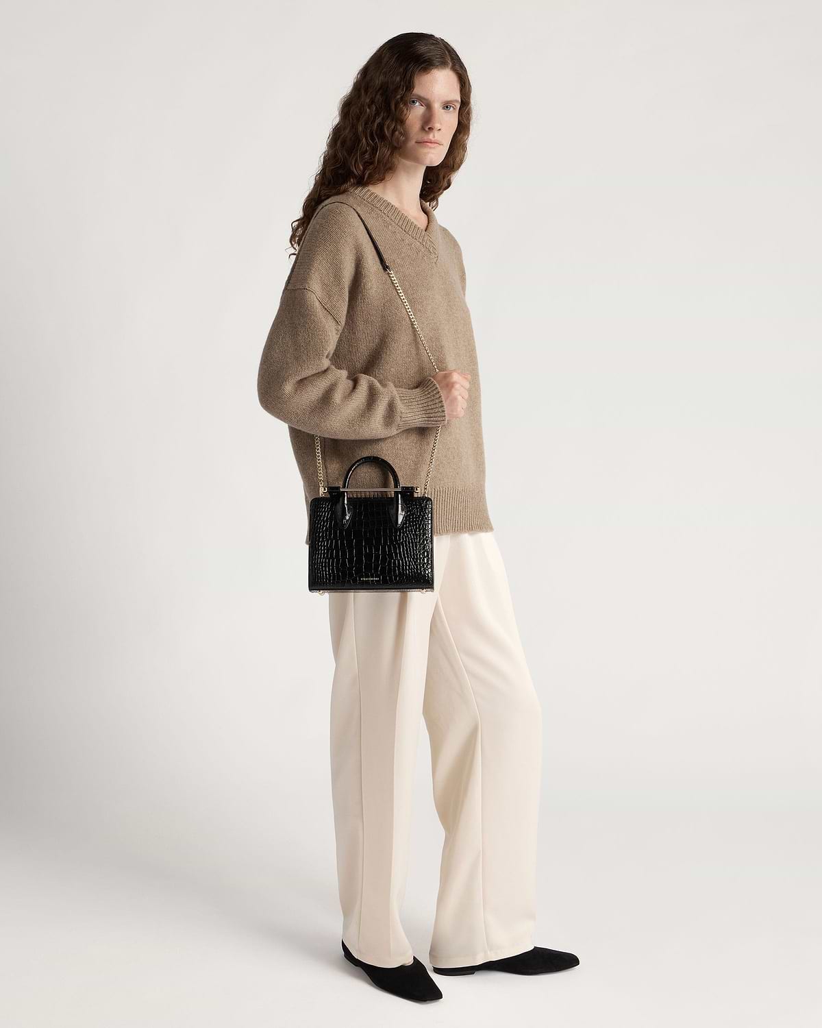 Model wearing beige jumper holding black croc mini tote with gold chain strap