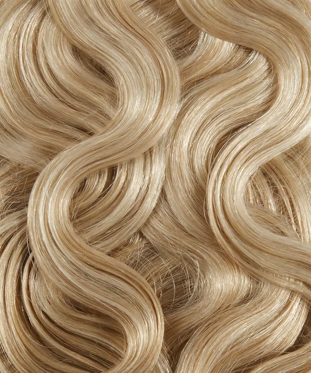 Close-up of wavy, blonde hair extensions with smooth, shiny strands, creating a textured pattern of flowing curves.
